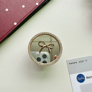 Close-up of a circular mirror phone stand with a golden bow and sparkling rhinestones