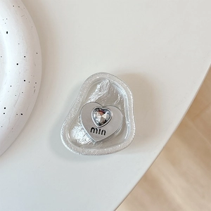 Detail of silver heart phone socket with crystal inlay and engraved logo on white stand