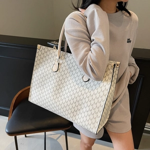 Vintage style cream tote bag with grey M pattern and gold hardware on female model