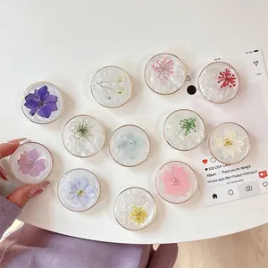 Glittery floral resin phone grip with real dried flowers and metallic rim on white surface