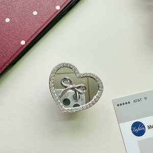 Macro detail of heart-shaped phone grip with silver bow, mirror surface and rhinestones