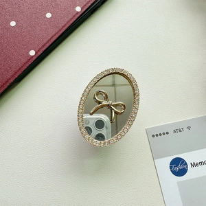 Detail of oval mirror phone grip featuring a gold bow and shimmering rhinestone border