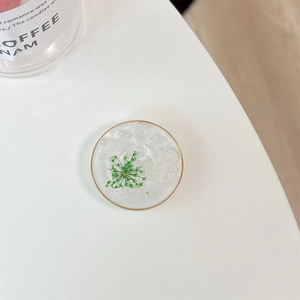 Detail of a round resin phone grip with real green dried flowers and gold foil accents
