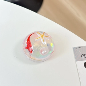 Macro shot of circular resin phone grip featuring a red fish, starfish, and pearl inside