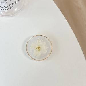 Macro shot of circular resin phone grip featuring white dried flower and gold rim