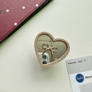 Macro view of heart-shaped phone grip with gold bow mirror and rhinestone borders