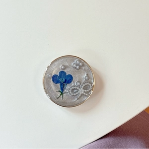 Gros plan d'une fleur séchée bleue avec nœud en perles dans une résine époxy pailletée