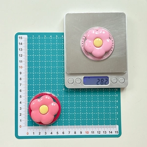 Detail showing weight and size of two pink flower-shaped phone grip sockets on a scale