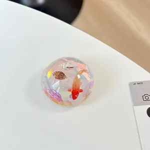 Detail of hemispherical phone grip featuring a miniature koi fish and seashell landscape