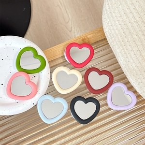 Silicone heart mirror phone stand in various matte colors displayed on a stylish tray