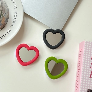 Three colorful heart-shaped mirror phone grips in red, black and green on a desk