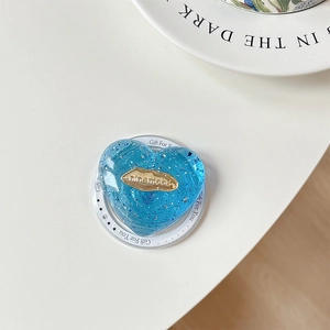 Close-up of heart-shaped blue resin phone grip with silver glitter and gold logo detail