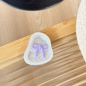 Détail du support MagSafe avec nœud violet et base nacrée sur une table en bois clair