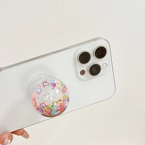 Makro-Detail des herzförmigen Handy-Halters mit bunten Pailletten auf einem weißen Handy