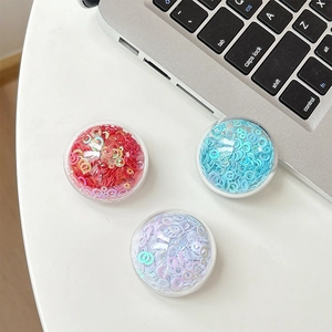 Close-up of three colorful sequin phone grip sockets on a desk near a laptop