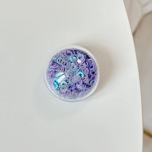 Macro shot of circular transparent box filled with iridescent purple sequins for DIY art