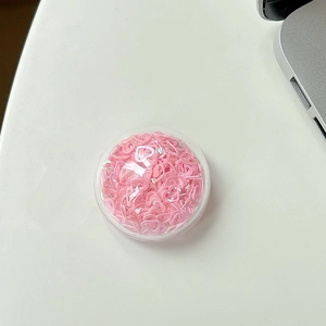 Nahaufnahme einer runden, klaren Handyhalterung mit schimmernden rosa Herz-Pailletten