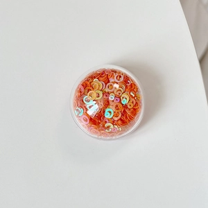 Close-up of bright orange and iridescent circular sequins in a clear round storage box