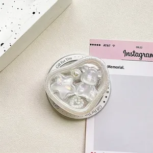 Detail of heart-shaped bear phone grip with iridescent stars on textured background