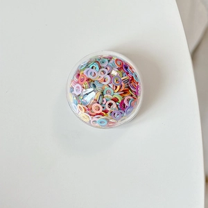 Close-up of a round phone socket grip filled with colorful confetti sequins on a white surface