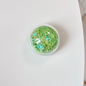 Detailed view of green hollow ring sequins in a round box for DIY phone grip decoration