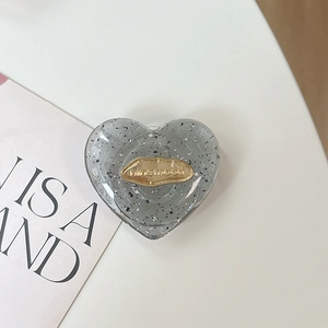 Dettaglio del supporto per telefono a cuore glitterato con placca in metallo dorato