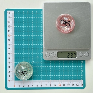 Detailed scale view of a round sequin phone grip with black bow design measuring 23.7g