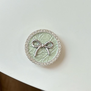 Detail of silver bow phone grip with sparkling rhinestones and green pleated leather texture