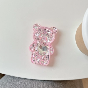 Support de téléphone ours rose pailleté avec miroir cœur et sequins sur table blanche