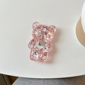 Détail du support téléphone ours rose pailleté avec sequins en cœur sur table blanche