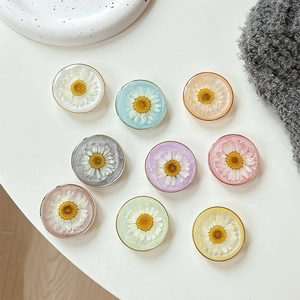 Daisy flower resin phone grip stand in various colors on a white minimalist desk