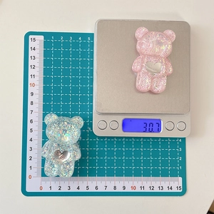 Close-up of glitter bear phone grips with heart mirror on green measurement mat and scale