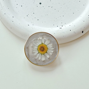 Close-up of a resin phone grip featuring an embedded real daisy and gold rim