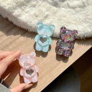 Close-up of bear-shaped phone grips with glitter heart cutouts on a sunny desktop