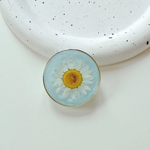 Macro detail of a resin phone grip with an embedded real white daisy and gold metal rim