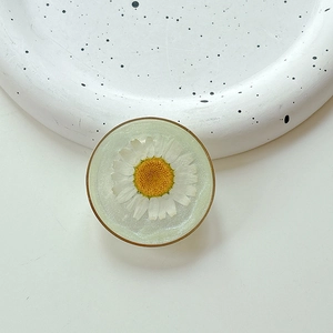 Detailed close-up of a resin phone grip with an embedded real white daisy and gold rim