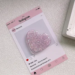 Détail d'un support de téléphone en cœur à paillettes roses sur un fond en marbre chic