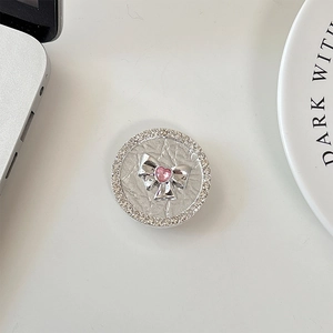 Close-up of rhinestone phone grip with silver bow and pink heart gem on white desk