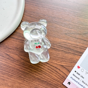 Close-up of transparent acrylic bear phone grip with red cherry pattern on wooden desk