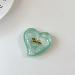 Détail du support de téléphone cœur pailleté vert clair avec emblème Smile doré sur blanc