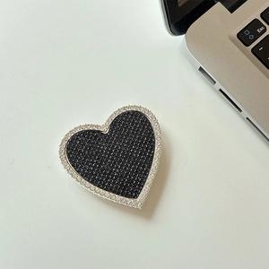 Dettaglio di un supporto per telefono a cuore con glitter neri e strass scintillanti sul tavolo