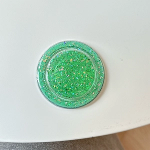 Close-up of circular MagSafe phone grip with green glitter and holographic sequins