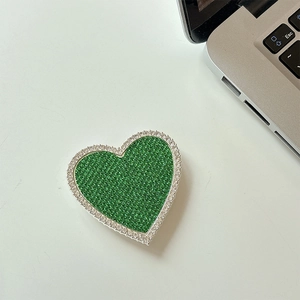 Dettaglio del supporto telefono a cuore verde smeraldo con strass su una scrivania bianca