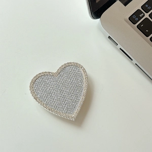 Dettaglio del supporto per telefono a cuore con strass scintillanti su tavolo bianco