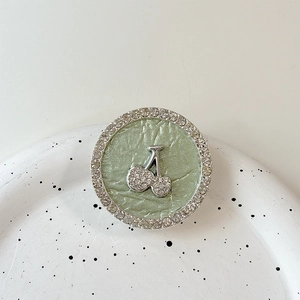 Detail of rhinestone cherry phone socket with green pleated texture and silver metal finish