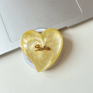 Detailed view of heart-shaped MagSafe phone grip with yellow glitter and Smile lettering