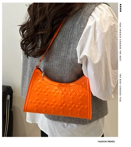 Detailed view of bright orange quilted crescent bag on model with gold hardware detail