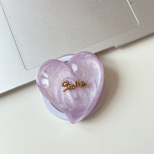Close-up of heart-shaped glitter phone grip with golden Smile lettering detail