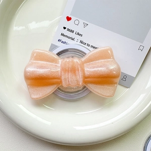 Macro view of pearlescent orange-pink glitter bow magnetic phone grip on ceramic plate