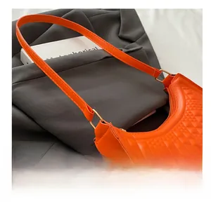 Close-up of orange baguette bag featuring quilted diamond pattern and gold metal ring link